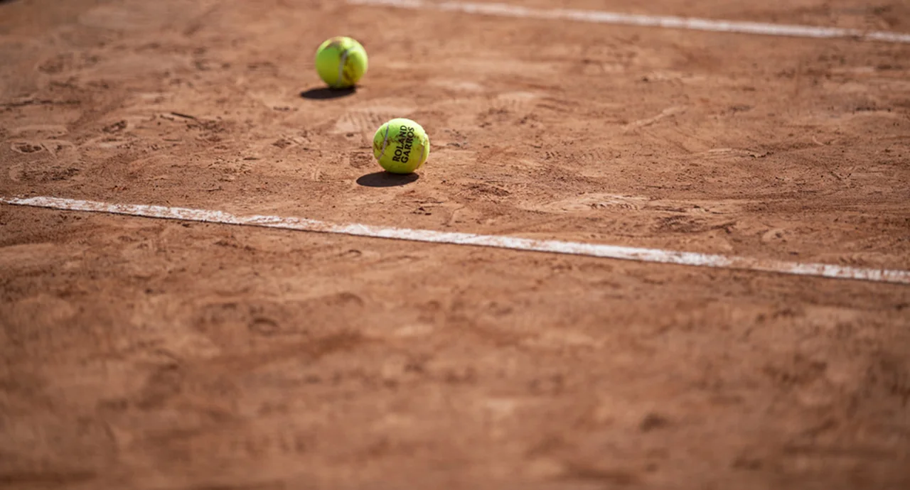 Two Roland-Garros tennis balls resting on a clay court